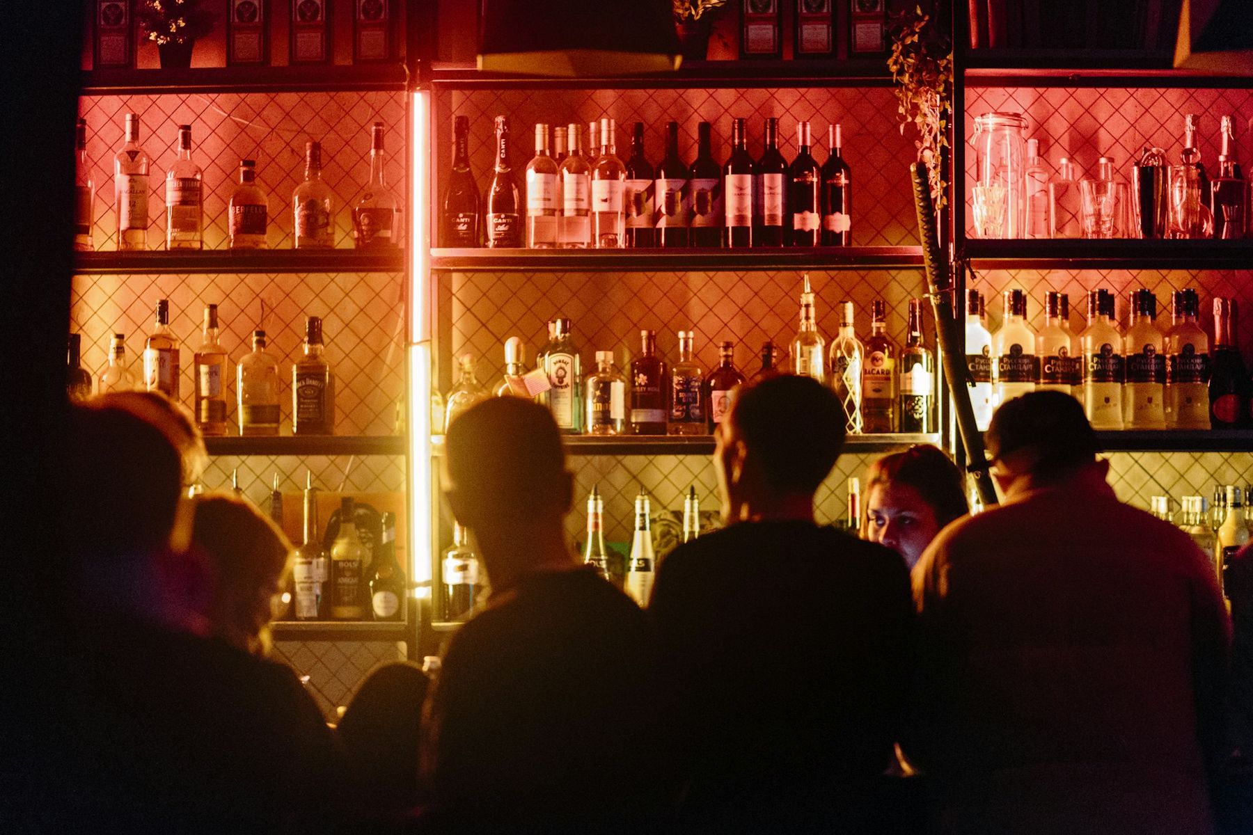 Guests crowded at a bar at night, lit by the back bar
